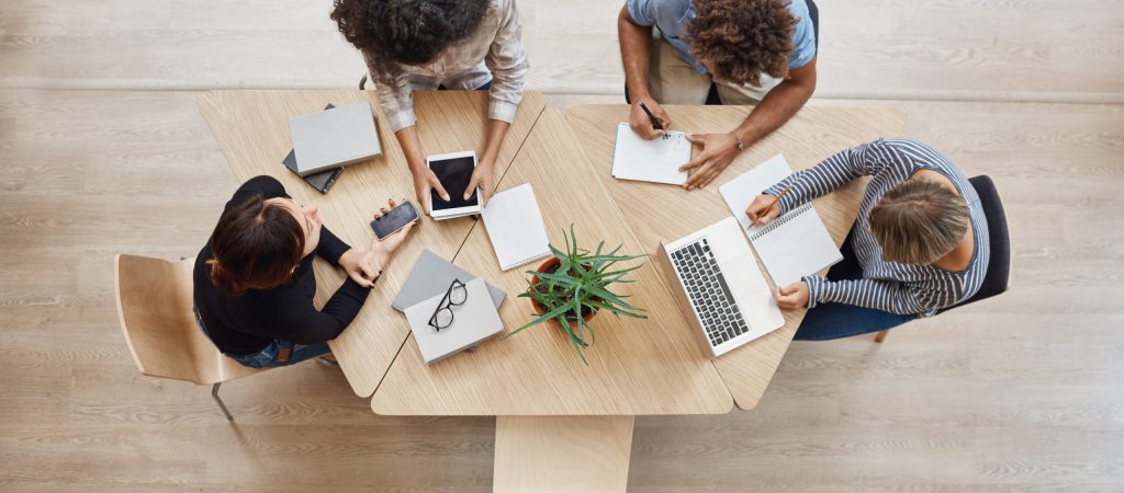 View from above. Business,startup, teamwork concept. Startup partners sitting at coworking space talking about future project, looking through examples of work on laptop and digital tablet